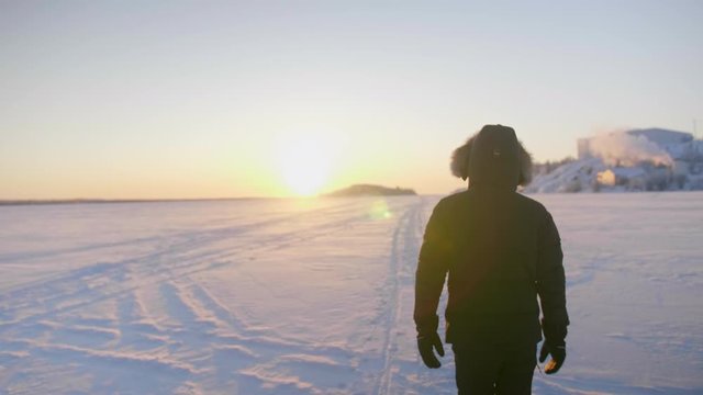 Slow motion of person walking away on deep snow into sunrise, canada