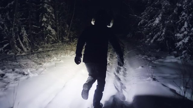 Person with flashlight run at night in deep snow forest, slow motion