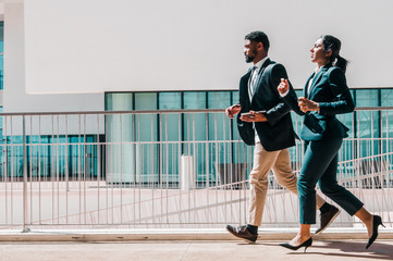 Business man and woman running outdoors. Business people wearing formal clothes with building in background. Business competition concept. Side view.