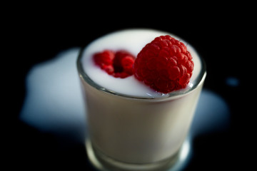raspberry fruit in a glass of milk on a black background