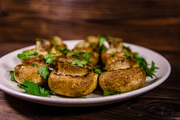 Plate with baked champignons, dill and parsley on a wooden table