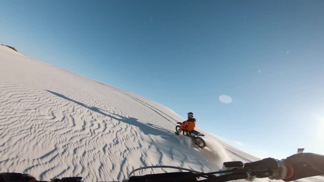 POV shot of dirt bikers in action on sand dunes. Two motocross riders racing bikes in desert.