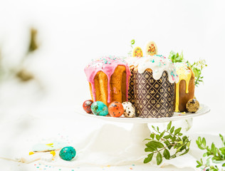Traditional Easter cakes, colored eggs and decor, green leaves on white background