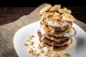 Oat pancakes with banana, yogurt and peanut on dark wooden background.