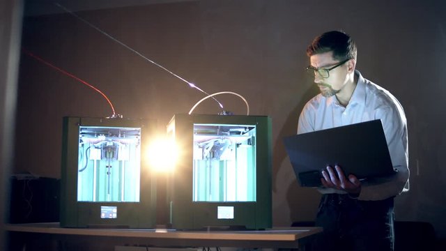 Two 3D-printers are working under supervision of a male expert