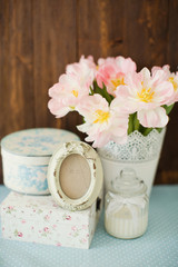 Vintage frame with bow decoration. Gift boxes with flower ornament. Bouquet of tulips with pink and white petals in white metal vase.