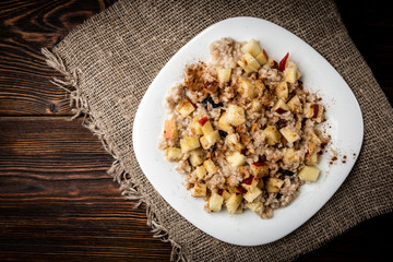 Oatmeal with honey, apple and cinnamon on dark wooden background.