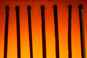 silhouette of seven matches with a red head in a row on a Lush Lava background. close up copy space
