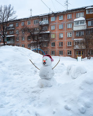 Winter cloudy day. Funny snowman stands in the courtyard of a residential building