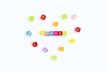 Top view on sign mother from small colorful letters and heart from colored letters with text love. Mother day card. Woman day. 8 march. Mothers day concept. White background.