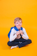 Little school boy with backpack sitting over orange background