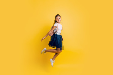 Obraz premium Happy excited teen schoolgirl happily jumps on a yellow background