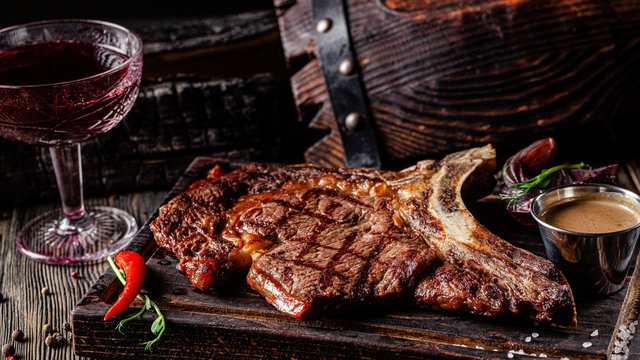 European cuisine in Ukrainian style. Large, juicy grilled T-Bone steak. Serving dishes in a restaurant on a wooden board with sauce. background image, copy space text