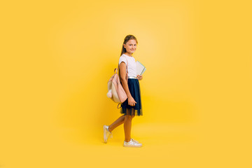 Fototapeta na wymiar A teenager with a backpack and books. Stylish beautiful schoolgirl posing on a yellow background