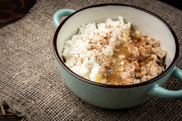 Oatmeal with honey, cottage cheese and cinnamon on dark wooden background.