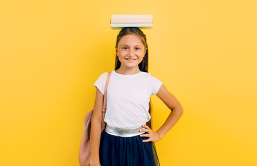 Positive teenage girl holding books on her head, on a yellow background