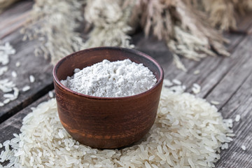 Rice flour in a bowl on a pile of white rice on old boards.