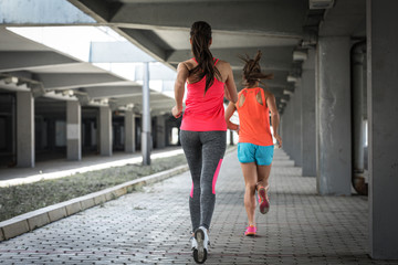 Two female runners jogging around the city road overpass.Urban workout concept.Rear view.