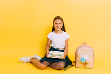 Happy teenage schoolgirl with books on a yellow background