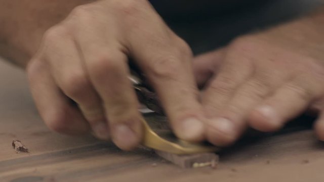 Craftsman uses plane tool to shave bowtie key in table top, close up slow motion