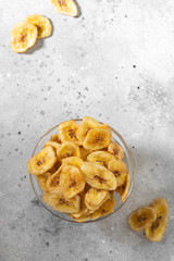 Dried bananas in a glass bowl on a gray kitchen table. Banana chips. Vegetarian snack for proper nutrition. Top view with space for text
