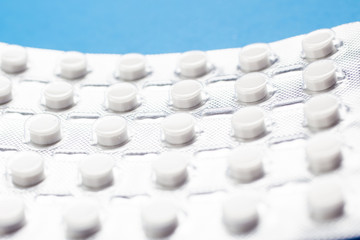 A lot of white tablets in silver pack on a blue background. Macro