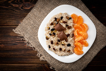 Oatmeal with mandarine, raisin, walnut and chocolate on dark wooden background.