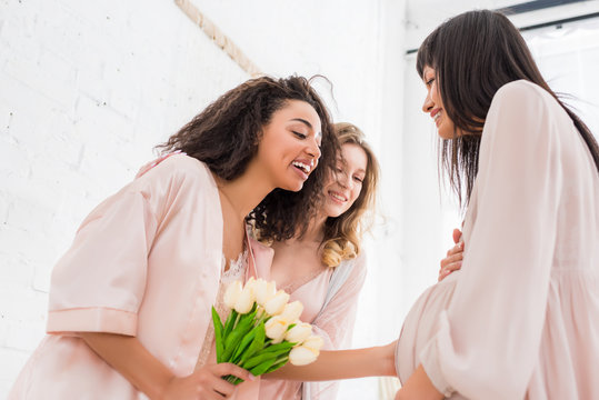 young pregnant woman with multiethnic girlfriends and tulip flowers on baby shower