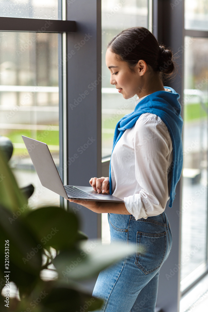 Wall mural Image of asian secretary woman holding laptop computer by window