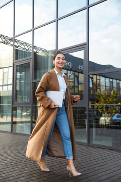 Image Of Young Brunette Asian Woman Holding Laptop While Walking