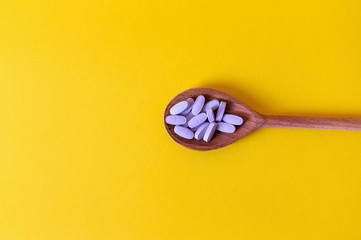 Vitamins in a wooden spoon on a yellow background.