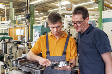 Fototapeta na wymiar A trainee in the metalworking industry and the instructor check a workpiece using a caliper