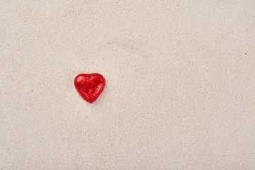 Chocolate red praline hearts on the beach sand on St. Valentine's Day