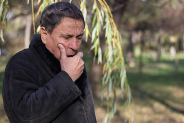 Portrait of a coughing senior man outdoors, looking down. Senior man having sickness, allergies