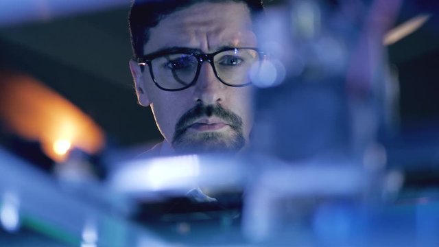 Man Working With A 3D Printer at 3d printing lab. Male specialist in glasses is observing a working mechanism