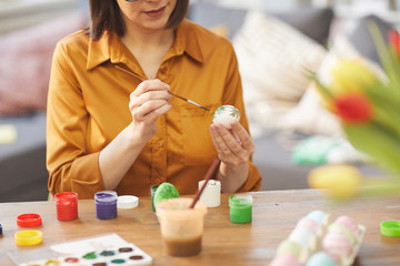 Close-up of young woman sitting at the table and painting eggs in colorful paints for Easter