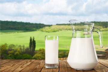A glass of milk and jug on wooden desk