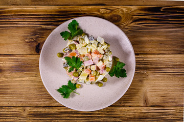 Ceramic plate with russian traditional new year salad olivier on a wooden table. Top view