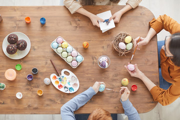 High angle view of family of three working at wooden table together they painting eggs for Easter holiday