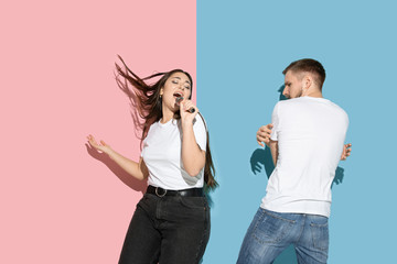 Spring season. Dancing, singing, having fun. Young, happy man and woman in casual on pink, blue bicolored background. Concept of human emotions, facial expession, relations, ad. Beautiful couple.