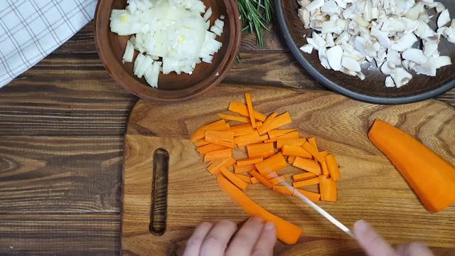 Slicing ingredients for a rice dish with vegetables. Vegetarian dish. Mushrooms and carrots onions. Healthy diet. On a wooden background.