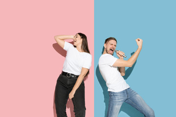 Sunny. Dancing, singing, having fun. Young and happy man and woman in casual clothes on pink, blue bicolored background. Concept of human emotions, facial expession, relations, ad. Beautiful couple.