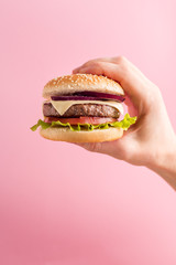 Man's hand holds burger on pink background