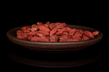 Lot of whole dried red goji with brown ceramic coaster isolated on black glass