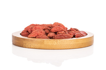 Lot of whole dried red goji on round bamboo coaster isolated on white background