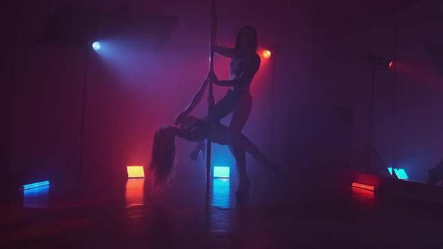 Sexy women pole dancing in dark studio with lights and smoke. Red and blue smoke. Females silhouettes dancing exotic dance in 4k, UHD