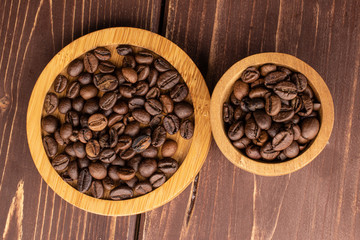 Lot of whole fresh coffee bean on round bamboo coaster in bamboo bowl flatlay on brown wood
