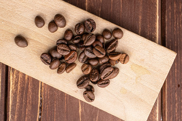 Lot of whole fresh coffee bean on wooden cutting board flatlay on brown wood