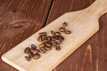 Lot of whole fresh coffee bean on wooden cutting board on brown wood