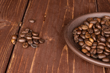 Lot of whole fresh coffee bean with brown ceramic coaster on brown wood